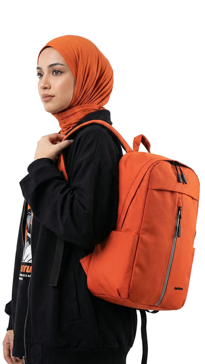 Person wearing an orange hijab and carrying an orange backpack on a white background