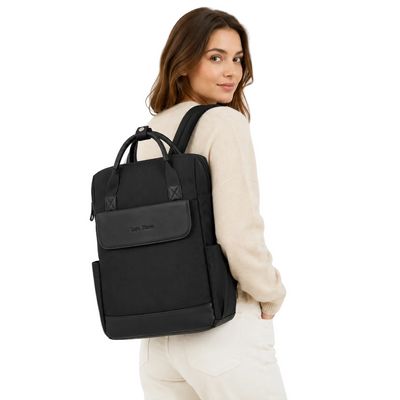 A woman wearing a cream-colored sweater and pants is shown from the back, carrying a black backpack with top handles and a front flap pocket. The brand name 'Lark & Linn' is subtly printed on the front pocket.